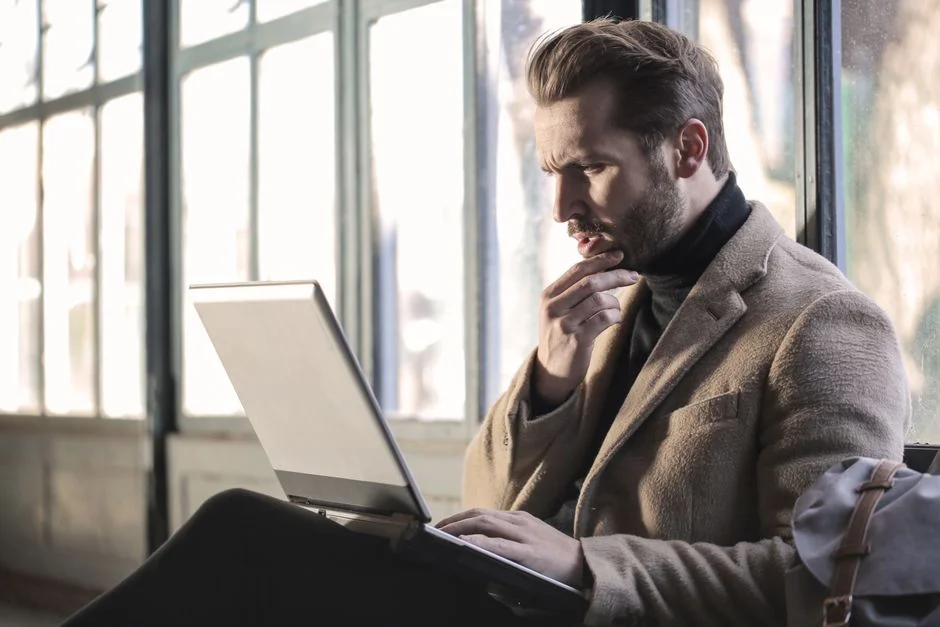 A man thoughtfully using a laptop while making a decision