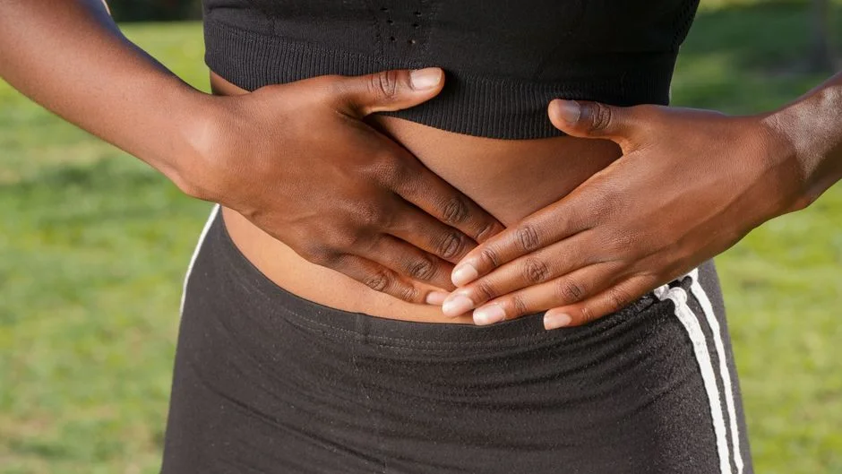 Close-up of a woman with her hands resting on her abdomen, representing gut health