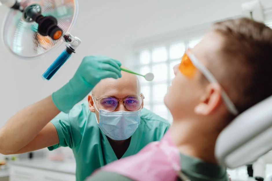 Dentist in surgical mask holding a dental mirror while examining a patient reclined in a dental chair