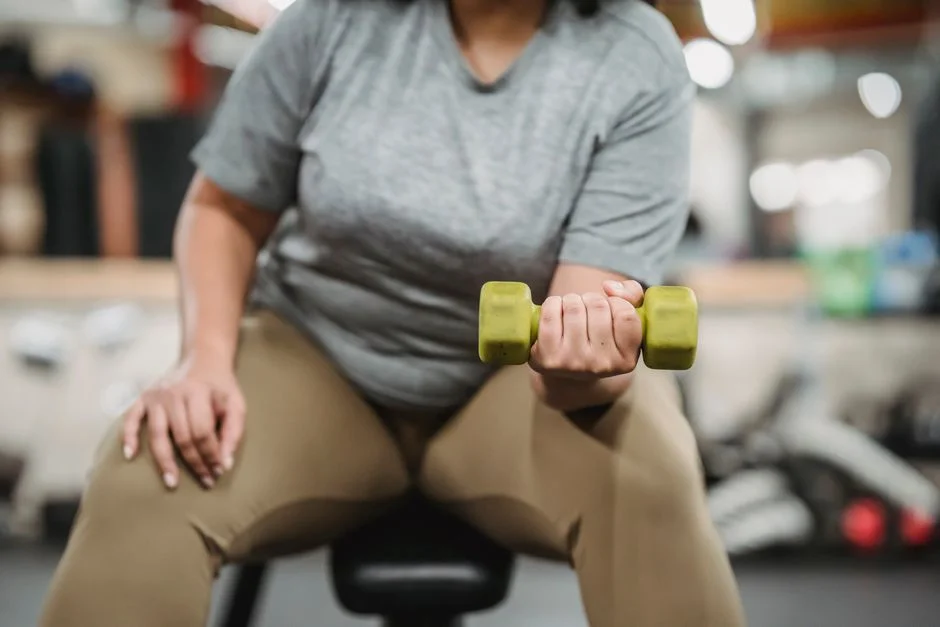 Seated woman in a gym performing a dumbbell curl with a green weight