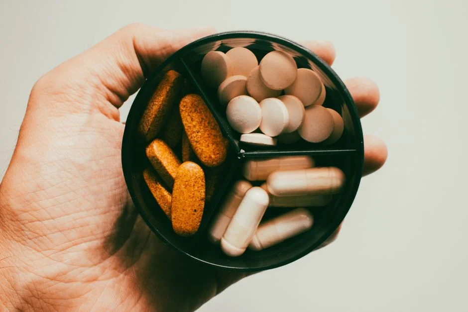 Open hand holding a round pill organizer filled with assorted supplement tablets and capsules