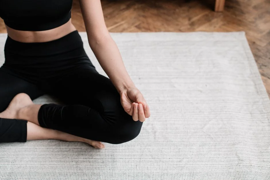 Person seated cross-legged on a rug with a hand resting on one knee in a meditation pose
