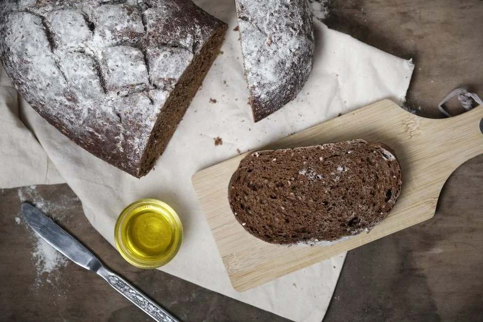 Slice of dark whole grain bread on a wooden board beside a small dish of olive oil