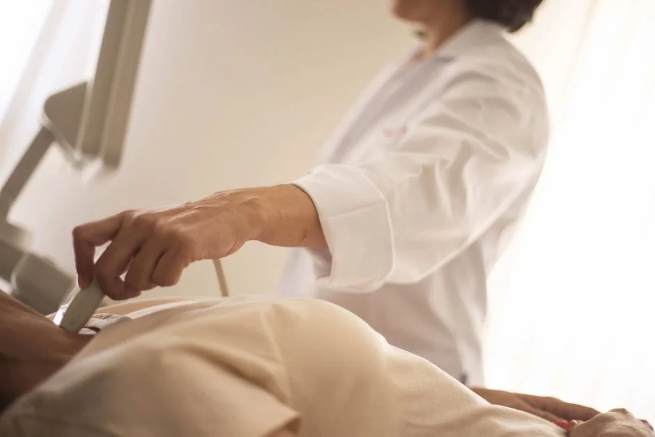 Clinician in a white coat guiding an ultrasound probe during a patient's exam in a clinic