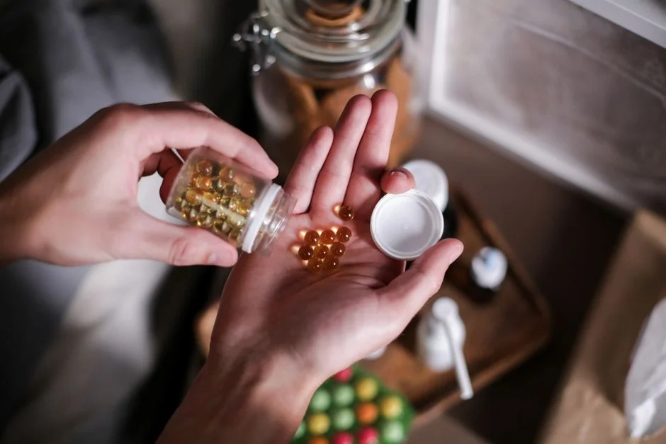 Hand holding amber softgel capsules poured from a small bottle