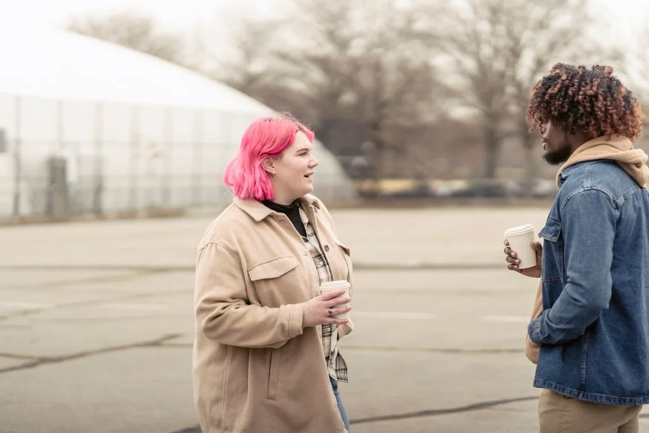 Two friends holding coffee cups and chatting outdoors on a cool day