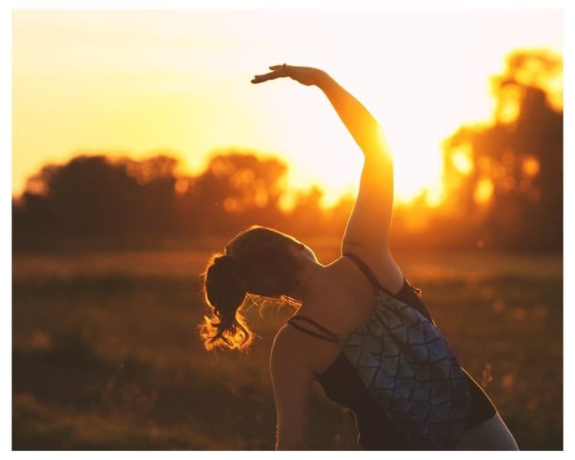Silhouette of a woman stretching one arm overhead in a field at golden hour